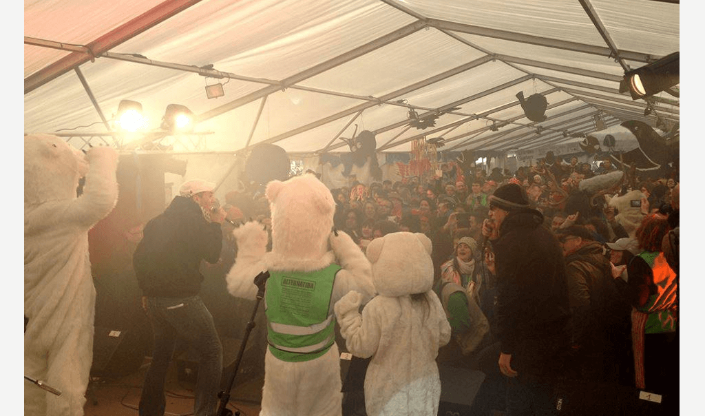 Personnes d'Alternatiba en combinaison d'ours sur scène devant une foule lors d'un concert du Village Mondial des Alternatives
