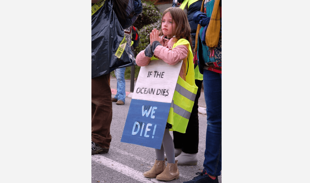 Petite fille les mains jointes portant une affiche "If the ocean dies, we die"