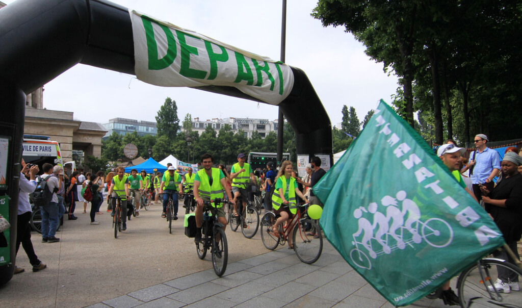 Des personnes à vélo commençant le Tour Alternatiba sous une bannière "Départ"