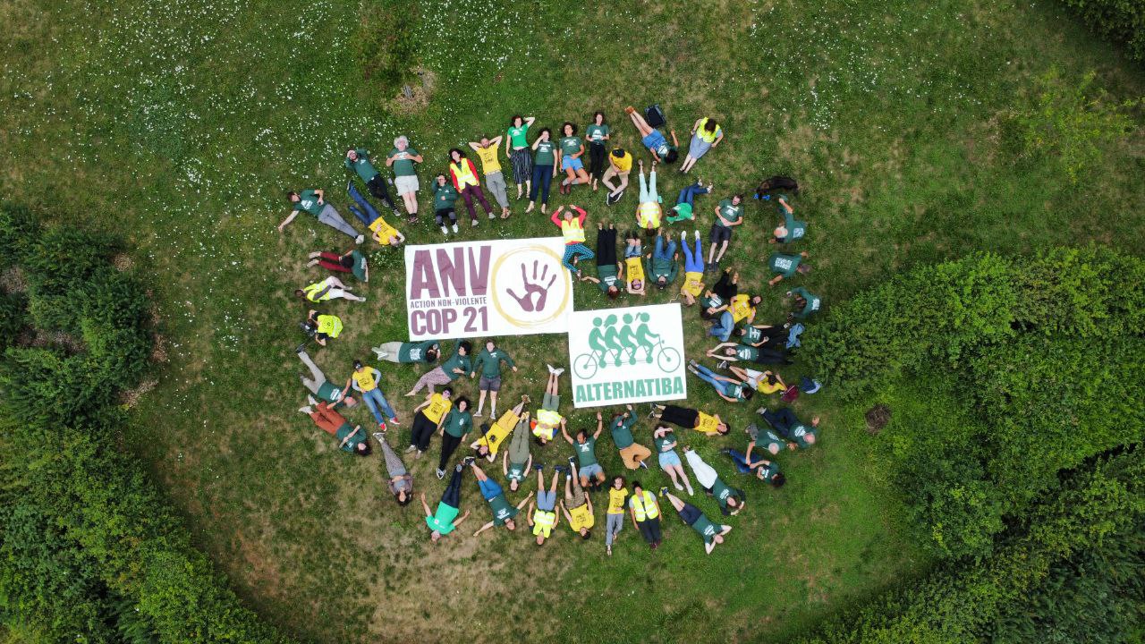 Vue depuis le ciel : deux bâches avec les logos Alternatiba et ANV-COP21 au centre et des personnes allongés autour