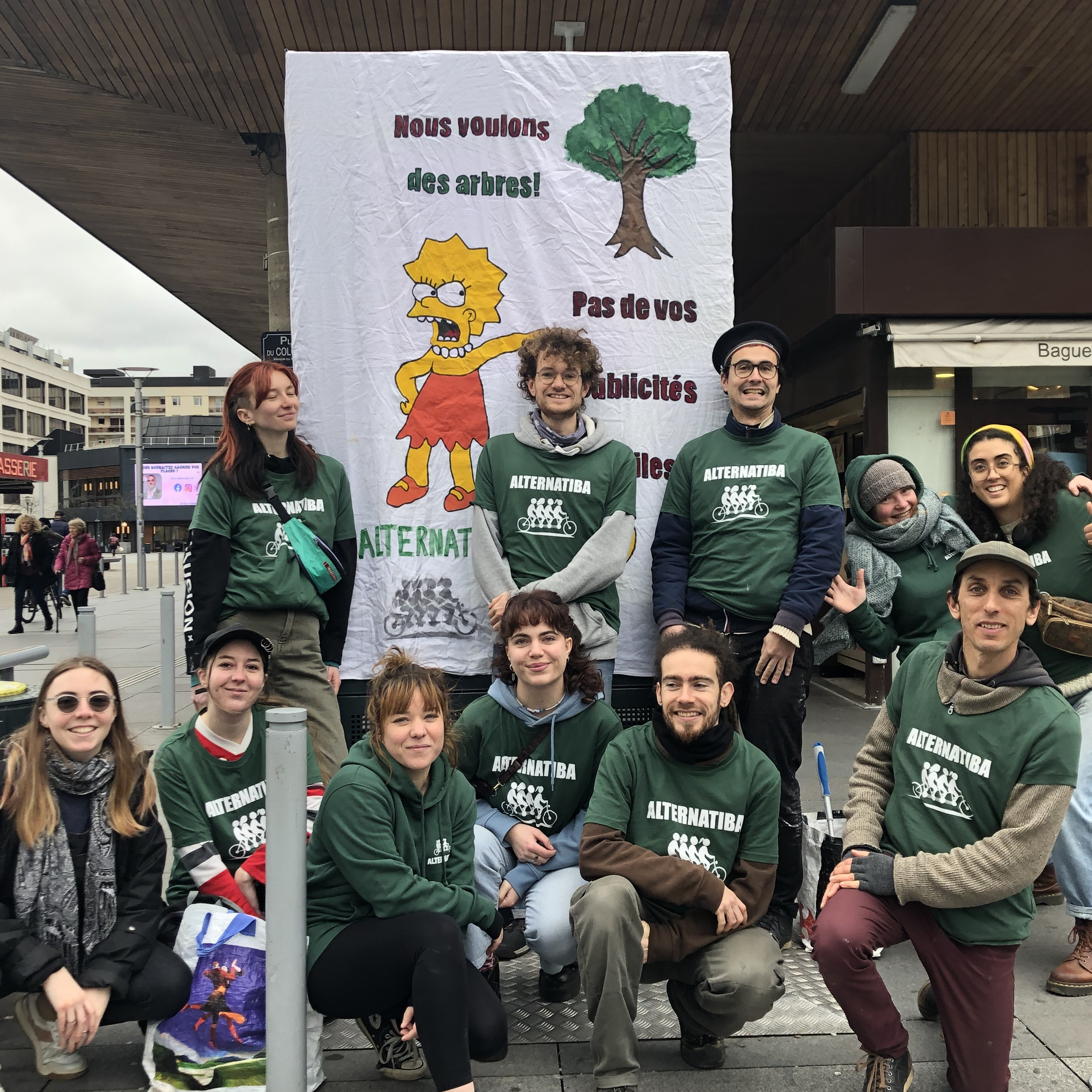 Photo de militant⋅es à Rennes posant devant un écran publicitaire recouvert : "Nous voulons des arbres, pas de vos publicités"